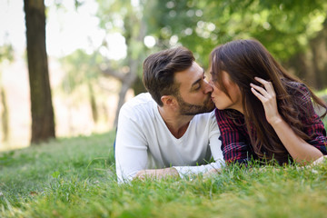 Wall Mural - Beautiful young couple laying on grass in an urban park.