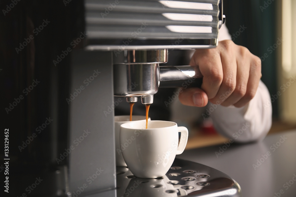 Male barista making fresh espresso in coffee maker, close up