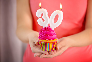 Wall Mural - Female hands holding birthday cupcake with candles, closeup