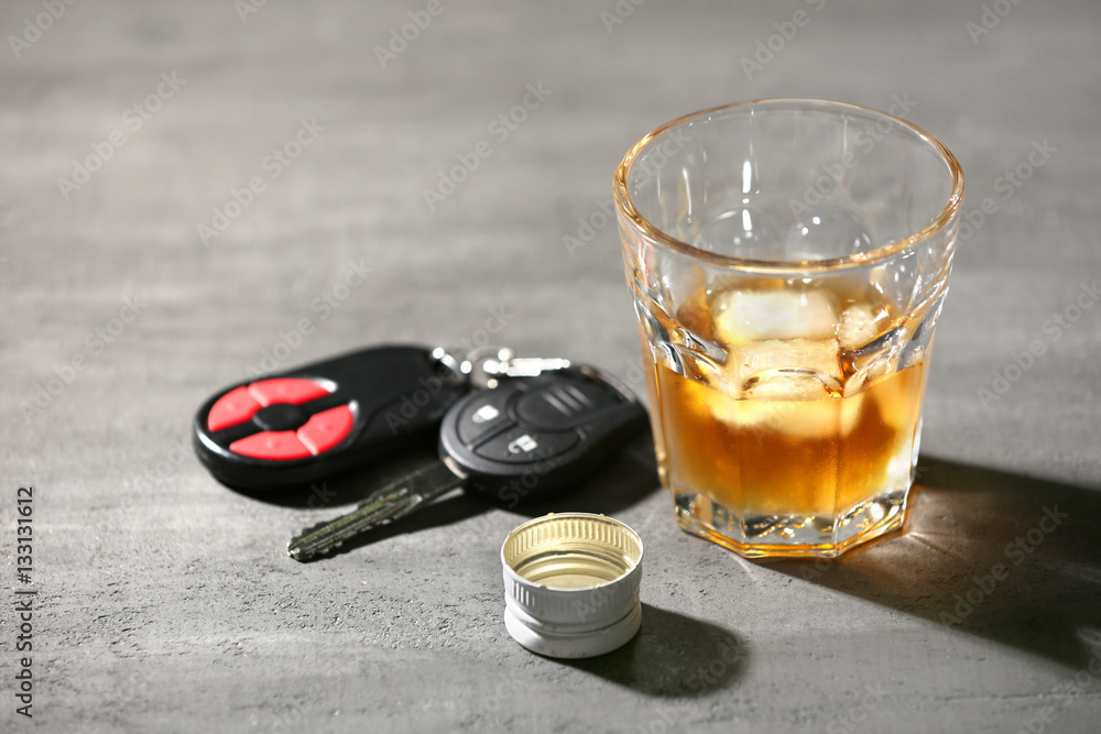 Glass with alcohol and car keys on grey table