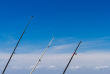 Three Fishing Rods Standing Against Blue Sky With Clouds