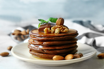 Delicious chocolate pancakes decorated with nuts and sweet syrup on plate