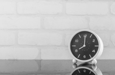 Wall Mural - Closeup black and white alarm clock for decorate in 8 o'clock on black glass table and white brick wall textured background in black and white tone with copy space