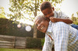 Young black boy climbing on his grandfather’s back in garden