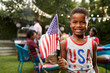 © Monkey Business - Young black boy holding flag at 4th July family garden party