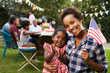 © Monkey Business - Black mother and baby hold flag at 4th July party, to camera