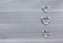 Three Small Hearts Of Multicolored Pebbles On Wooden Surface. Ba