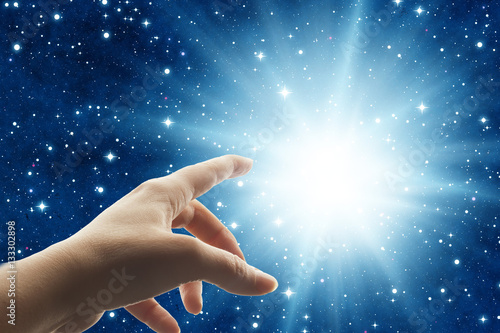 Fotografie, Obraz woman hand touching a divine light in the universe like a spiritual mystical con