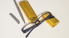 Black Glasses, Gold Case And Pen On The White Background