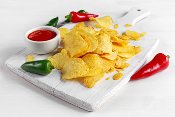 Gold and Crispy Potato Chips with hot sauce on white board, background.