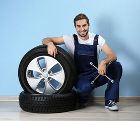 Young mechanic in uniform with spanner and wheels, on blue background