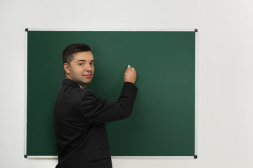 Canvas Print - Handsome young teacher writing on blackboard in classroom