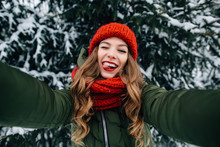 Winter Selfie. Young Happy Girl In Red Knitted Hat And Scarf Takes Selfie And Play The Ape In Winter Cold Day. Girl Takes Winter Selfie
