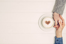Couple In Love Holding Hands With Coffee On White Wooden Table. Photograph Taken From Above, Top View With Copy Space