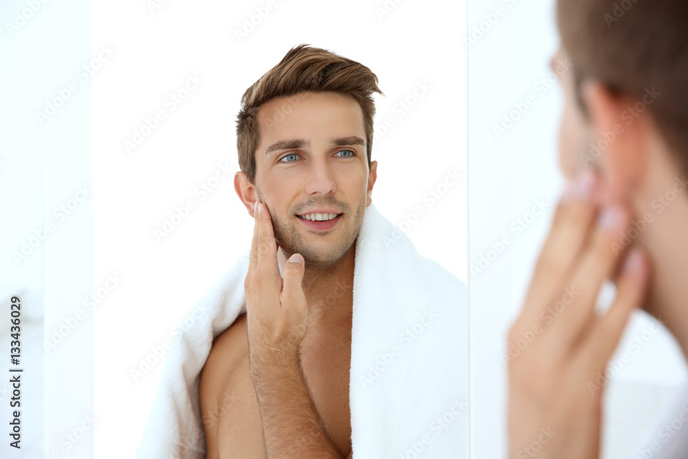 Young man standing in front of mirror and touching his face