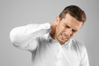 © Africa Studio - Young man suffering from pain in neck on grey background