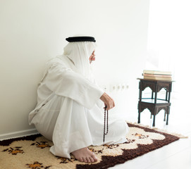 Arabic aged man sitting on ground using traditional beads