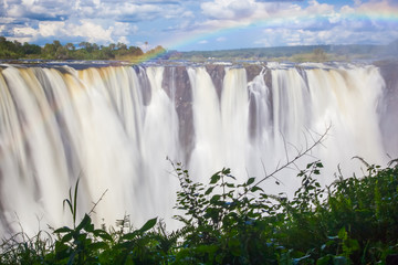 Wall Mural - Victoria Falls, a frontal view with a rainbow through the mist and spray.