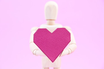 Wooden dummy holding paper box red heart shape on pink backgroun