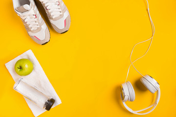 Athlete's set with female clothing, headphones and bottle of water on yellow background