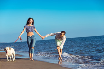 two young people running on the beach kissing and holding tight with dog