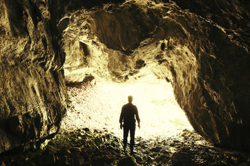Wall Mural - Cave exploring. Man silhouette at cave entrance with sunlight entering the dark cave tunnel, underground landscape, potholing adventure