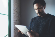 Closeup View Of Pensive Bearded African Man Using Tablet While Standing Near The Window In His Modern Apartment.Concept Young Business People Working At Home.Blurred Background.