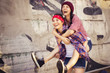 Two Brunette teenage girls friends in hipster outfit (jeans shorts, keds, plaid shirt, hat) with a skateboard at the park outdoors. Copy space