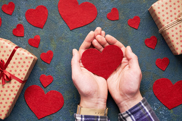 Wall Mural - Heart in the men's hands of love. Concrete background with hearts and gifts on Valentine's Day. Symbol of love. The concept of a romantic Valentines Day. Flat lay. Top view table.