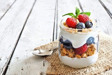 Wall Mural - healthy blueberry and raspberry parfait in a mason jar on a rustic white wood background