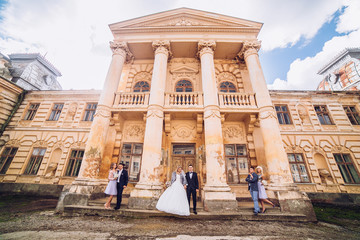 Wall Mural - bride and groom with bridesmaids and groomsman near old castle with columns jumping and embracing together.