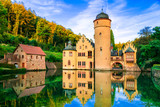 Moated castle Mespelbrunn with water reflection and stone bridge, Bavaria, Germany. Late medieval architecture in Spessart forest.