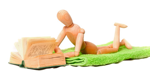 wooden mannequin on lies on a towel and reads the book