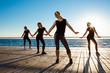 © Cookie Studio - Silhouettes of sportive girls dancing zumba near sea at sunrise.