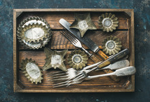 Old Vintage Tin Baking Molds And Cutlery In Rustic Wooden Tray Over Dark Blue Shabby Background, Top View, Horizontal