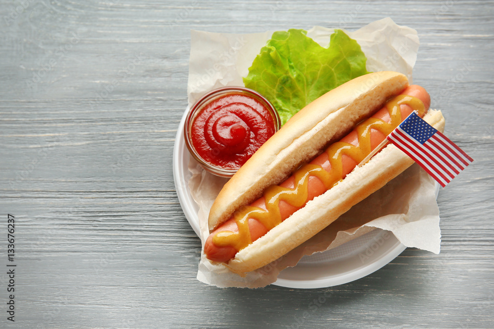 Tasty hot dog with American flag on table