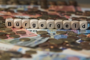 Wall Mural - bürgergeld - Holzwürfel mit Buchstaben im Hintergrund mit Geld, Geldscheine