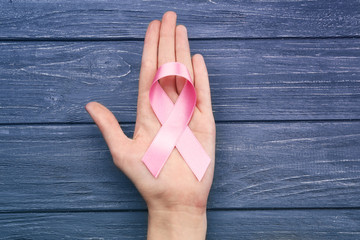 Wall Mural - Female hand holding pink ribbon on grey wooden background. Breast cancer concept