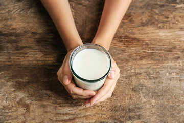 Wall Mural - Female hands holding glass of milk on blurred wooden background, closeup