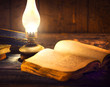 Old books and vintage oil lamp. Kerosene lantern and open old book on wooden table