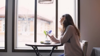 Poster - Side view of a young woman sitting at the table in cafe and texting on mobile phone 