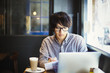 © Mint Images - Young Japanese man enjoying a day out in London, sitting in a cafe, using laptop computer.