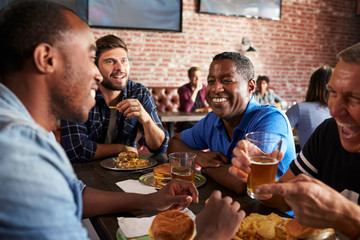 Wall Mural - Male Friends Eating Out In Sports Bar With Screens In Behind