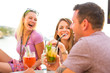 © Connect Images - Three adult friends laughing over cocktails at waterfront restaurant, Majorca, Spain