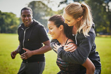Personal Trainer Encouraging Two Women Piggy Backing In Park