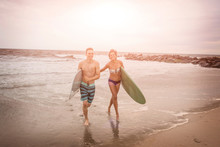 Young Surfing Couple Carrying Surfboards On Rockaway Beach, New York State, USA