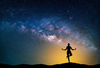 Wall Mural - landscape with milky way galaxy. night sky with stars and silhouette woman practicing yoga on the mo