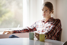 Thoughtful Man Holding Coffee Mug While Sitting By Window At Home