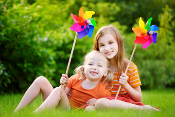 Two cute little girls holding colorful toy pinwheels on sunny summer day