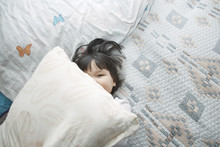 Overhead View Of Girl Peeking Over Pillow At Home